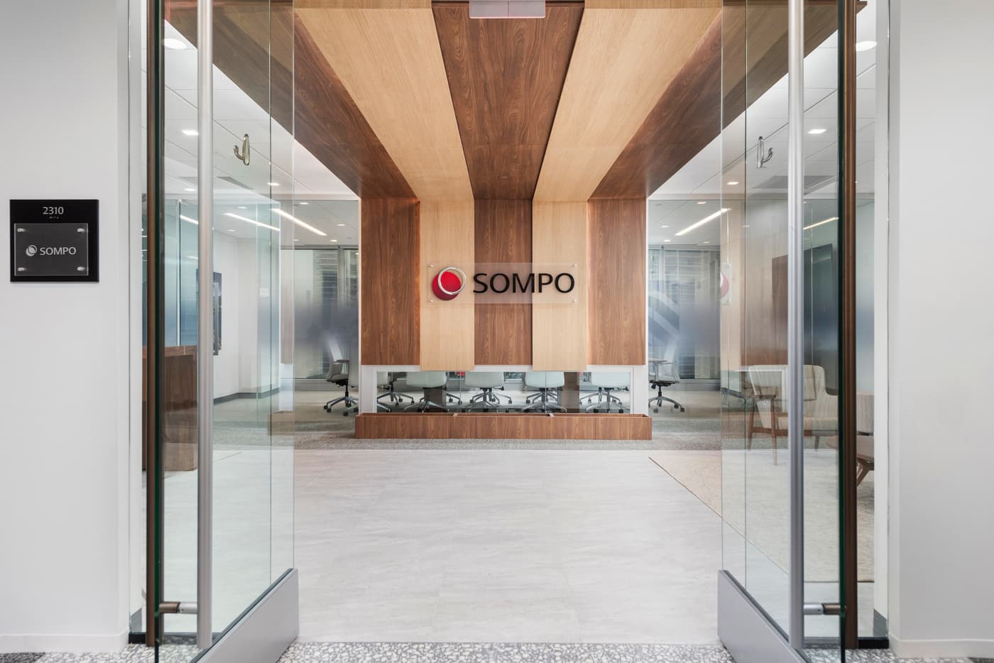 Sompo International's Miami office: reception lounge beneath a folded walnut ceiling with the Sompo wall sign, photograph 2