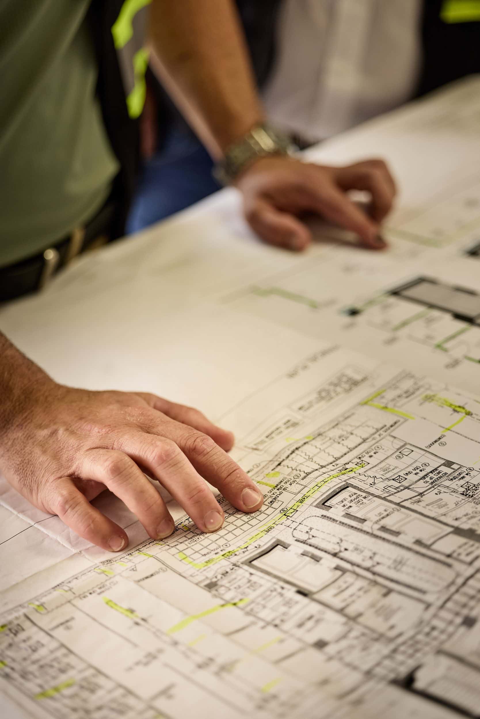 Hands resting on an open set of construction drawings marked in green highlighter