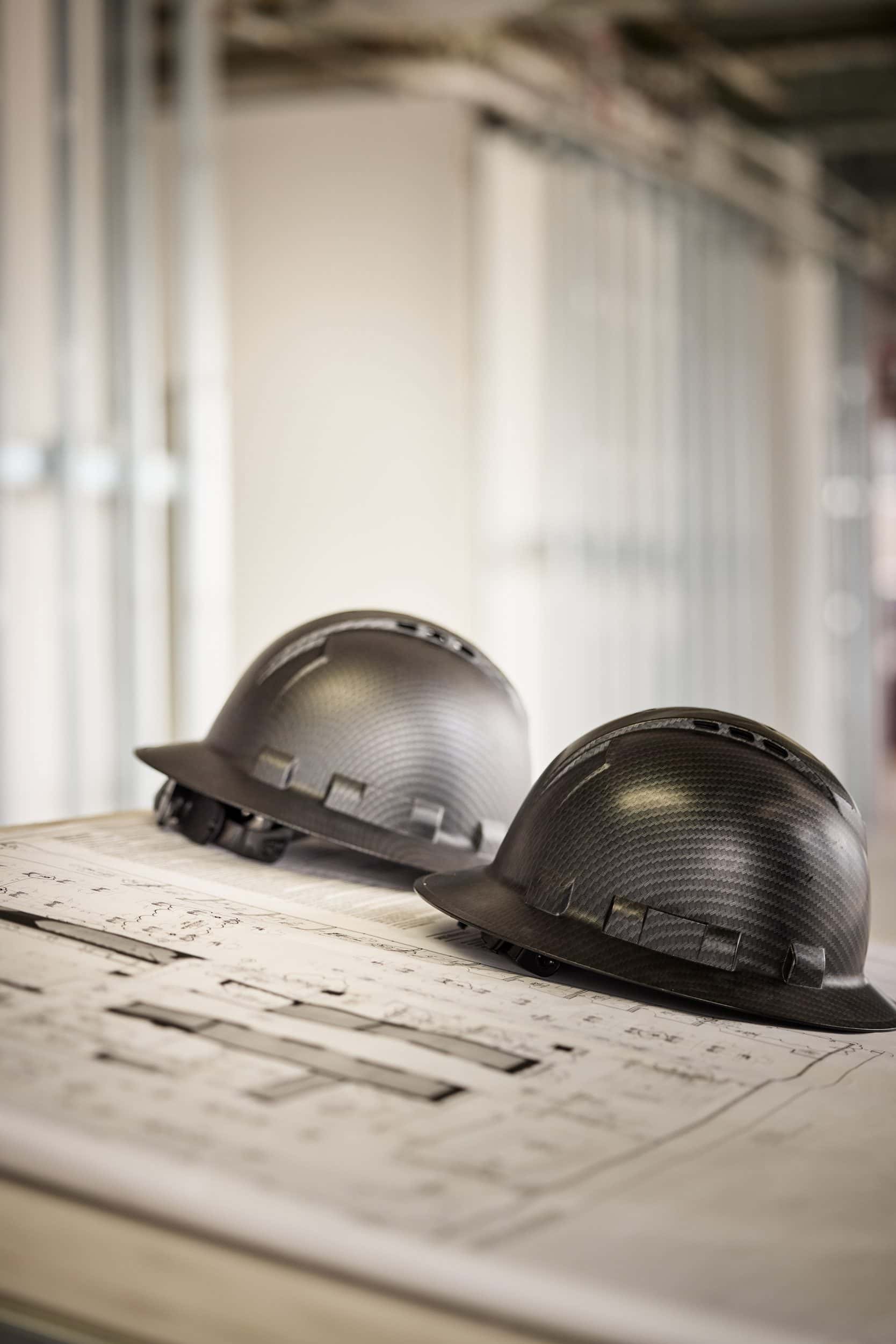 Two black SPARC hard hats resting on a set of drawings on a plan table
