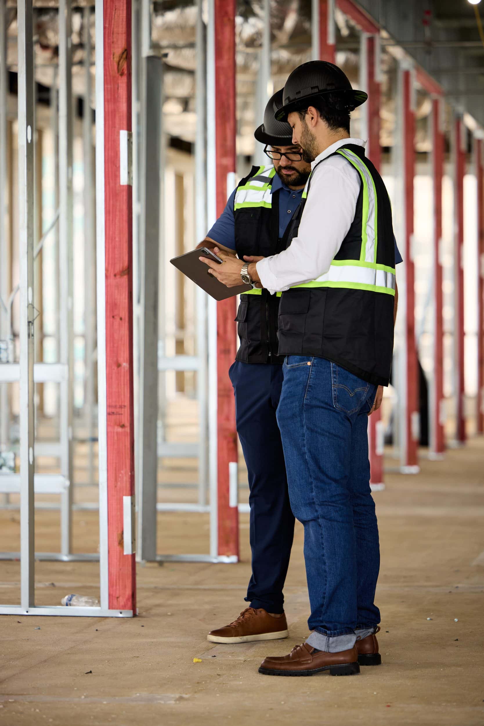 Two project managers in hi-vis vests reviewing a tablet together on a jobsite